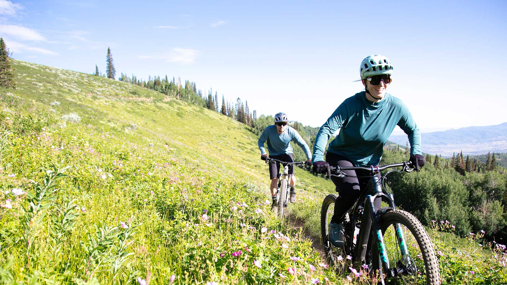 Jans Experts riding mountain bikes on a trail on a grassy hillside with a clear blue sky at Deer Valley Resort, Park City, Utah.