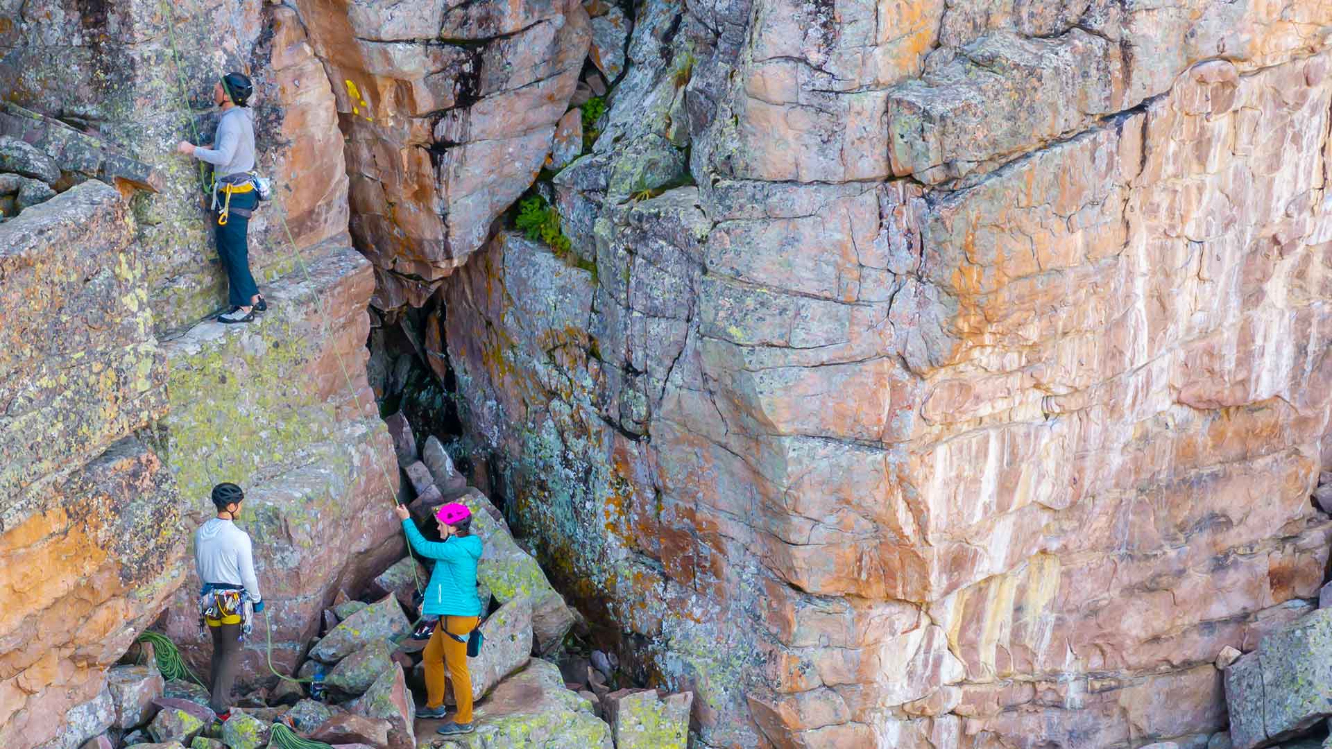 Three people exploring a rocky crevice between large stone formations.