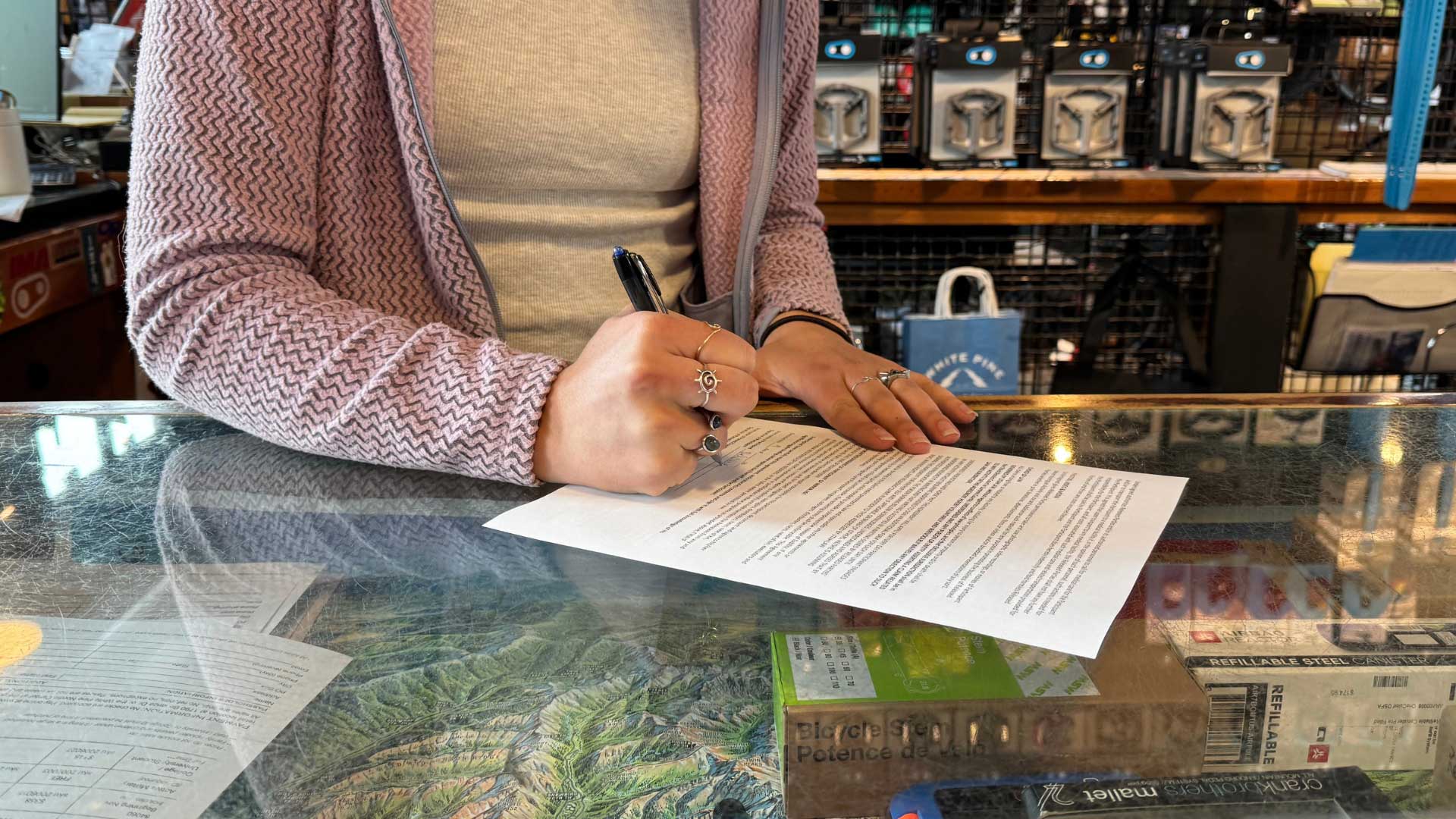 Person signing a document at a counter with a store setting in the background