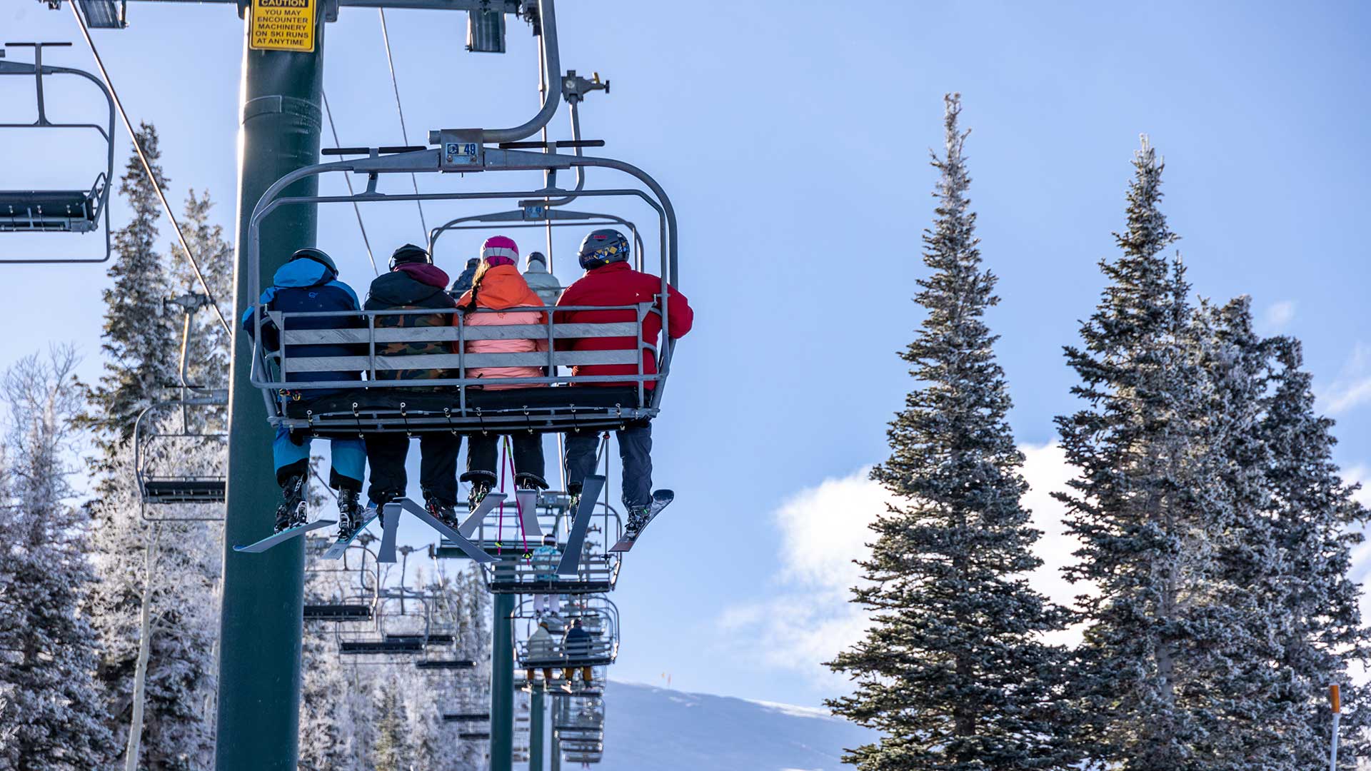 People on a ski lift with snow-covered trees and mountains in the background