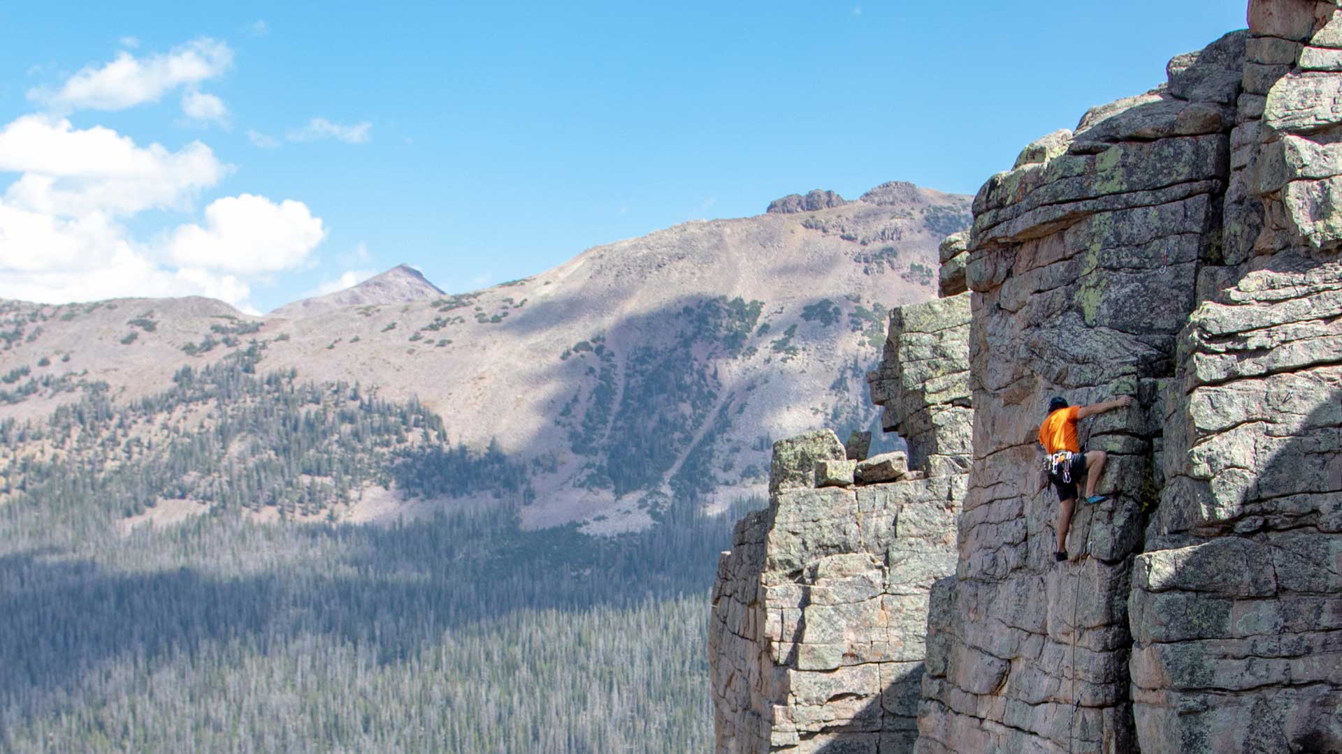 Person climbing a rocky cliff with mountains in the background