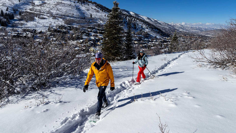 Jans Expert leading a snowshoe tour on a snow-covered trail overlooking Park City, Utah.