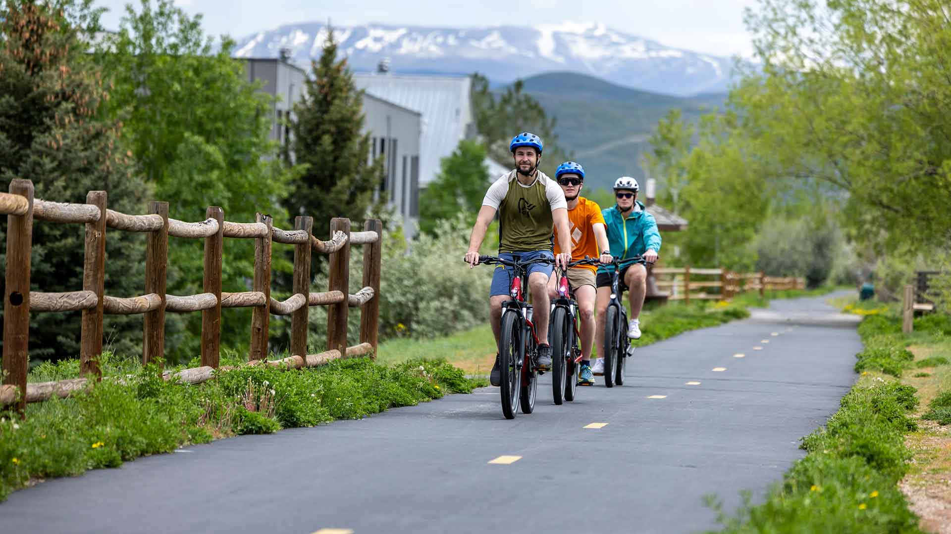 Three people riding bicycles on a paved trail with mountains in the background