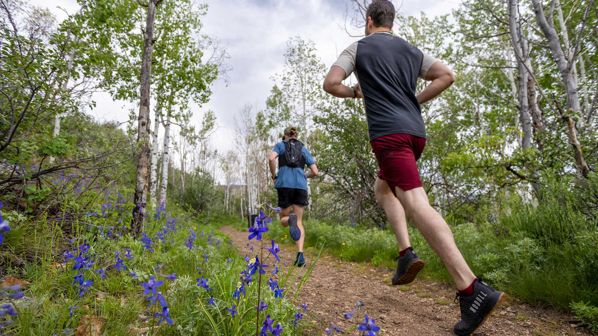 Two people running on a trail with trees and flowers in the background