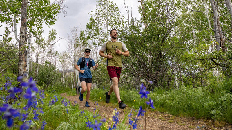 Two runners on a trail with trees and flowers in the background