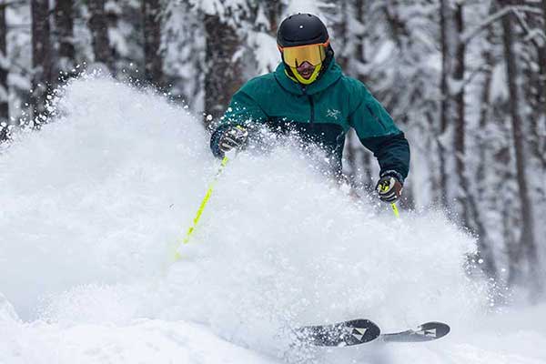 Jans Expert skiing through deep powder with trees in the background and powder kicking up over his waist at Deer Valley Resort, Park City, Utah.