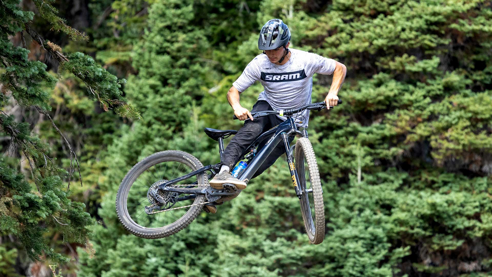 Person riding a mountain bike in mid-air with trees in the background