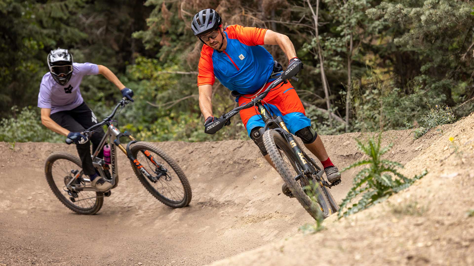 Two mountain bikers riding on a dirt trail in a forested area.
