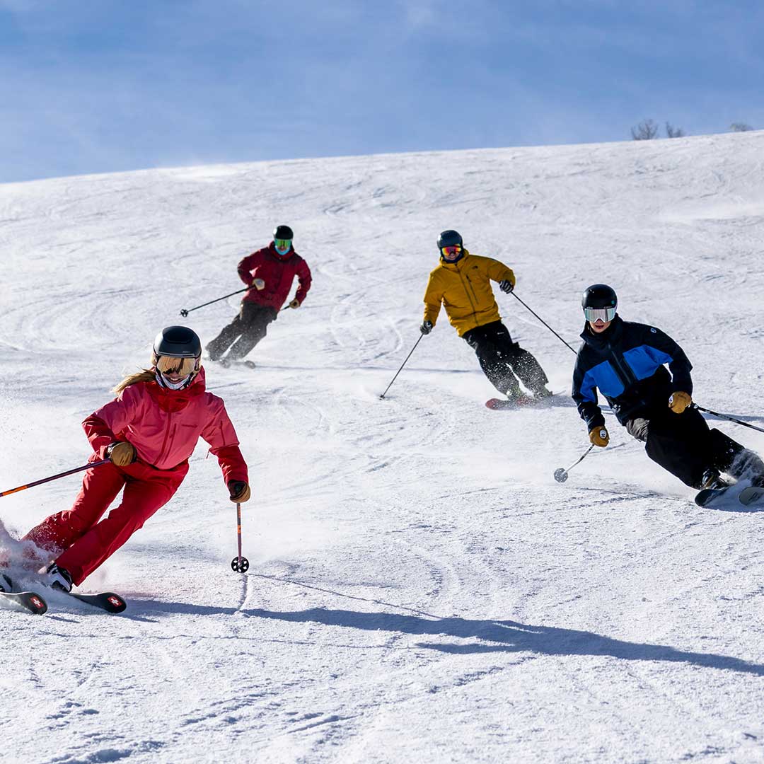 Four expert skiers from the Jans team skiing on a groomed run during a blue-sky day at Deer Valley Resort, Park City, UT