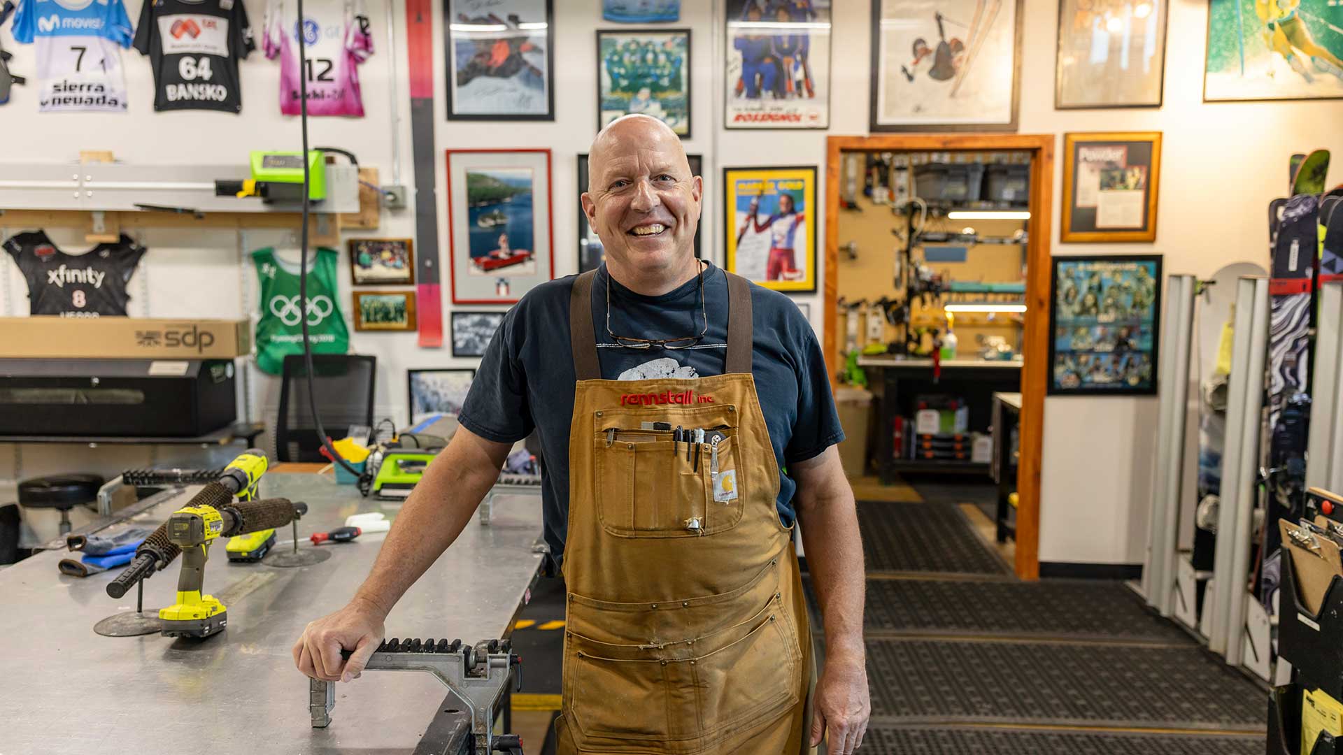 Rennstall manager, Andy Buckley wearing a brown leather bib apron over a dark t-shirt stands in the Rennstall Tech Center in Park City, Utah.