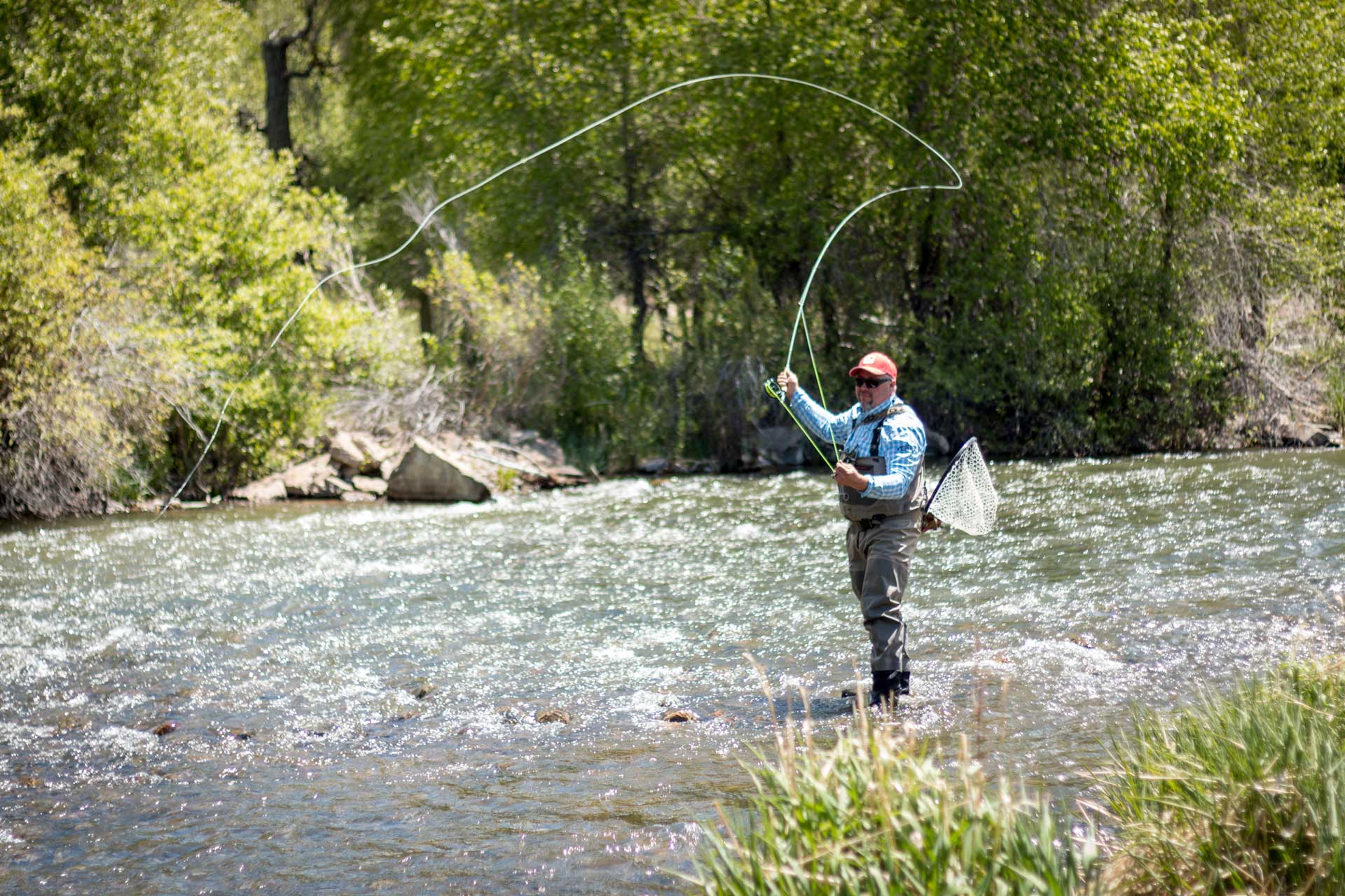 Person fly fishing in a river with trees and rocks in the background