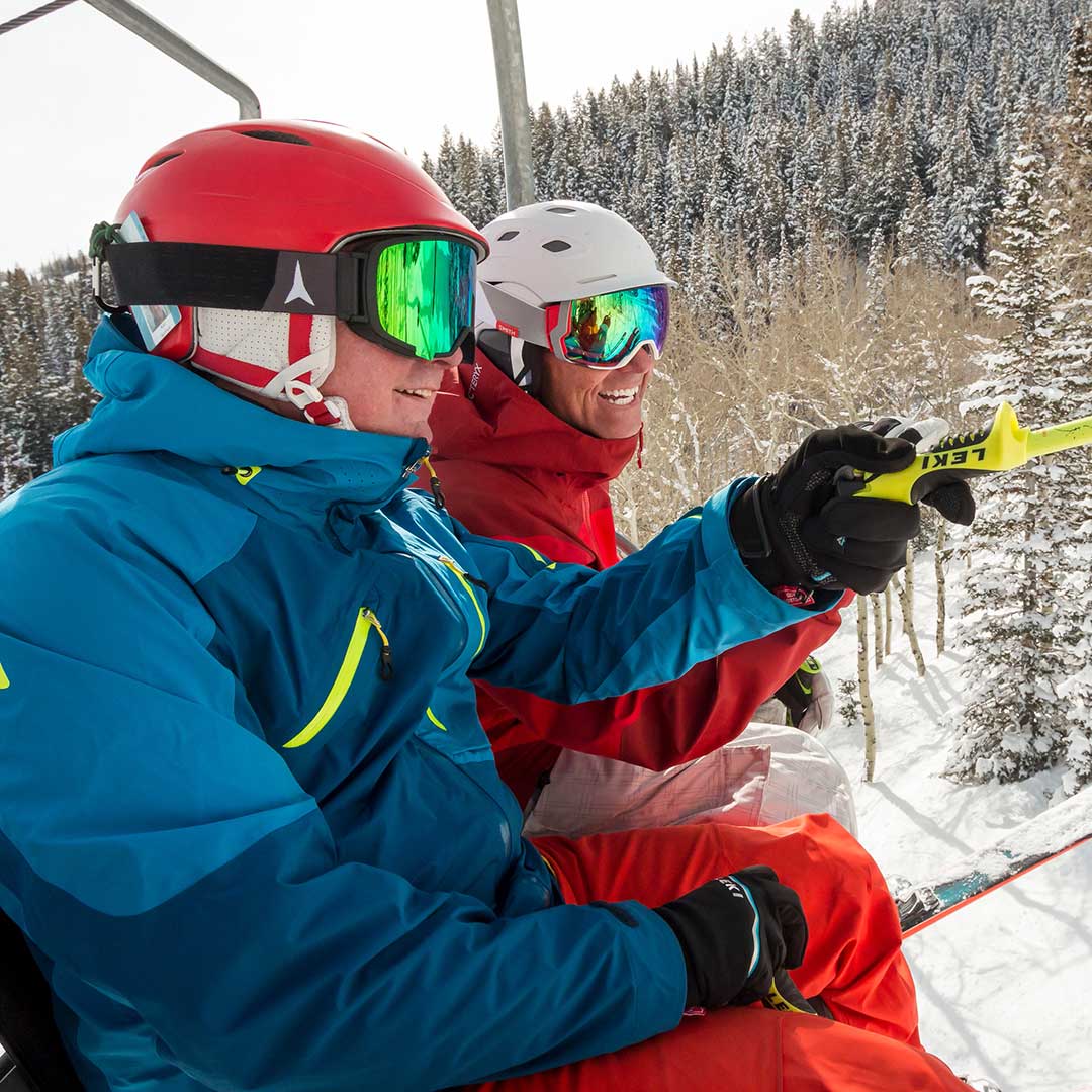 Two skiers on a chairlift with snow-covered trees in the background