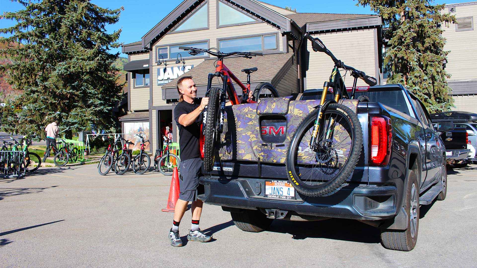 Man loading bicycles onto a truck with a building and trees in the background
