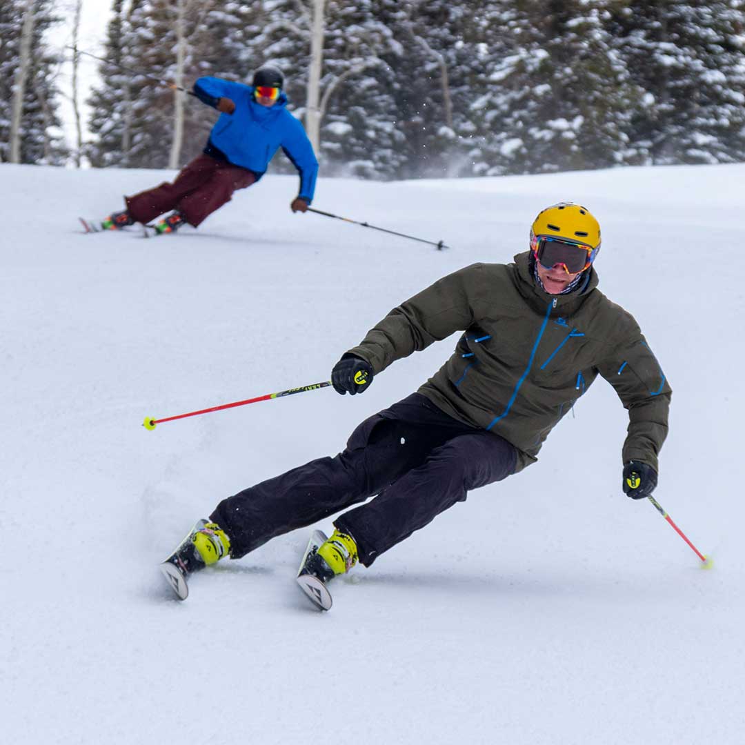 Two skiers in action on a snowy slope with trees in the background