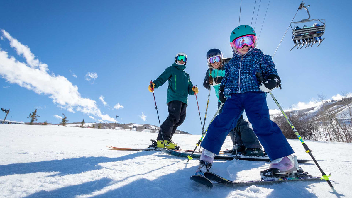 Jans Experts skiing with their child on a groomed run with a chairlift overhead at a Park City, Utah