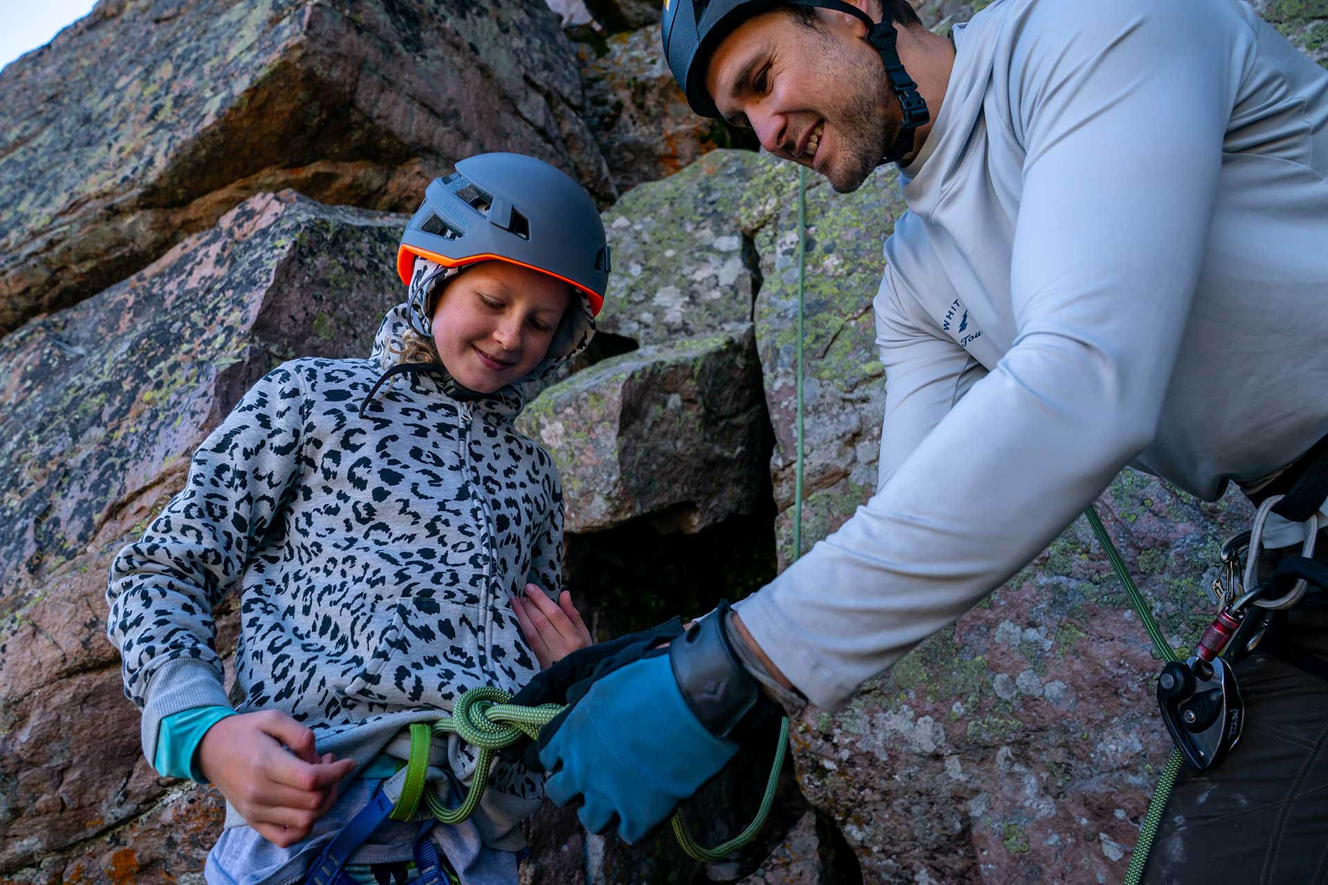 Person assisting another person with climbing gear on a rocky outdoor setting