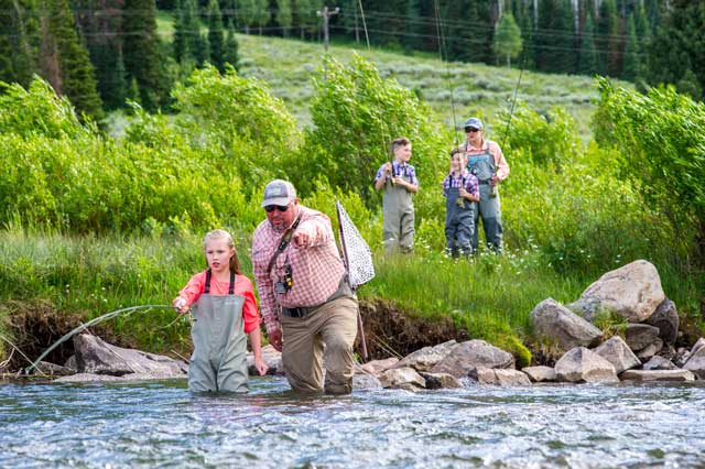 People fishing in a river with greenery and rocks in the background