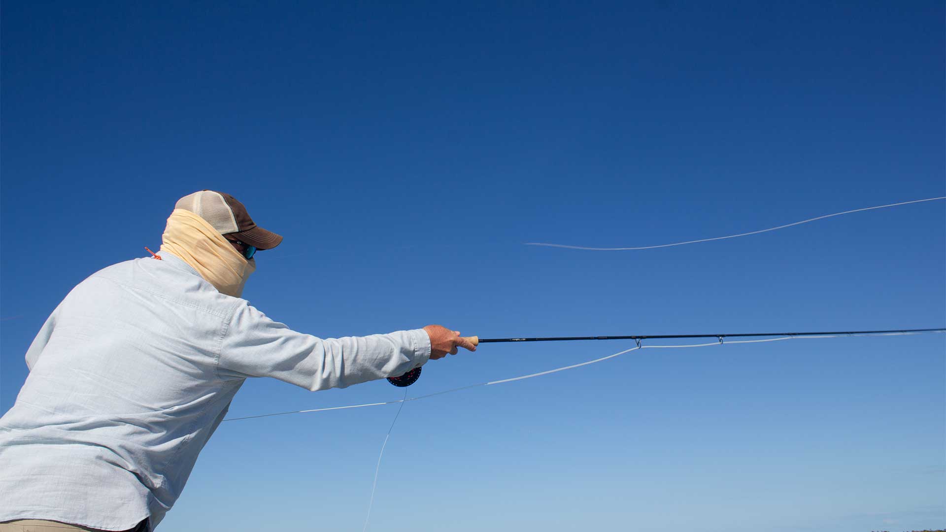 Person fly fishing against a clear blue sky