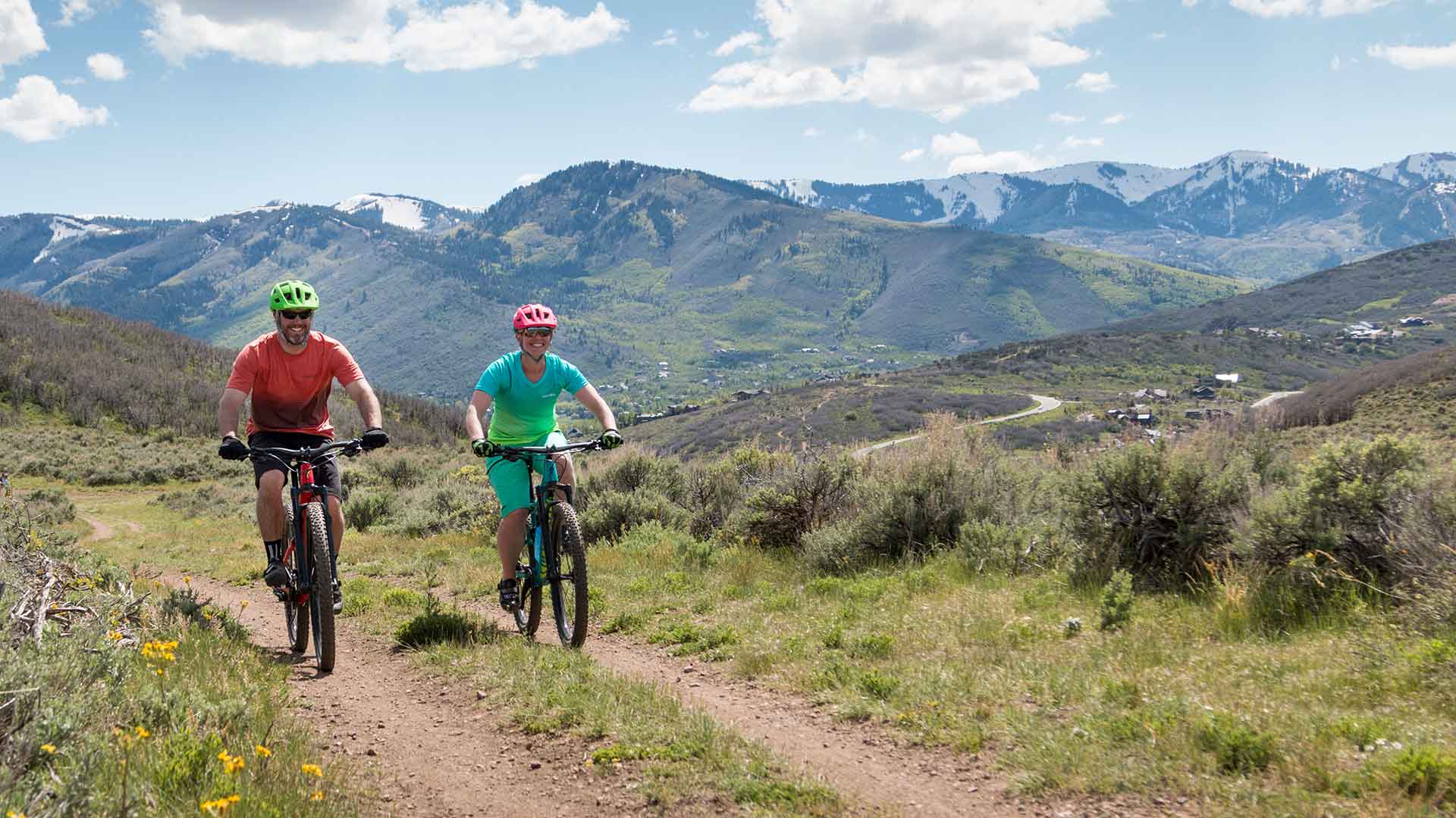 Two people mountain biking on a trail with mountains in the background