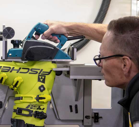 Person using a power tool with a focus on safety gear, wearing a yellow Fischeri jacket.