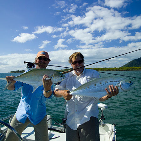 Two people on a boat holding fish with a scenic background