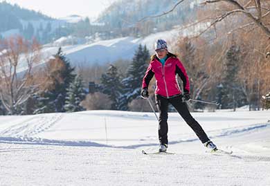 Person cross-country skiing on a snow-covered trail with mountains in the background