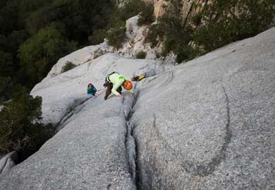 Person climbing a rocky mountain face with safety gear.