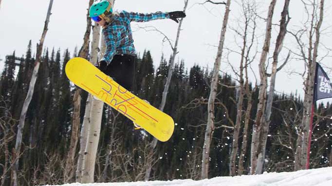 Person snowboarding in a snowy landscape with trees and a banner in the background