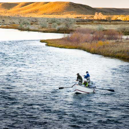 Two people in a small boat on a river with a scenic landscape.