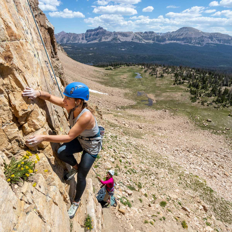 Person climbing a rocky mountain with another climber in the background