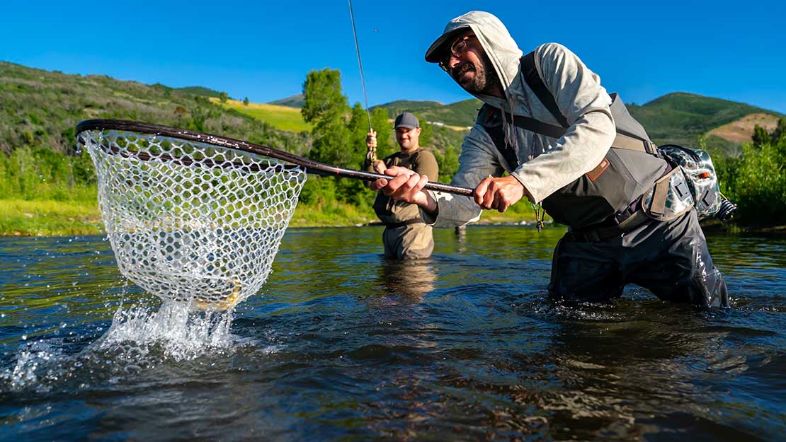 Two people fishing in a river with one person holding a net.