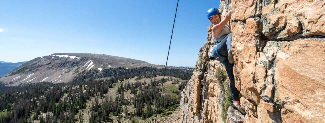 Person climbing a rocky mountain with a scenic landscape in the background