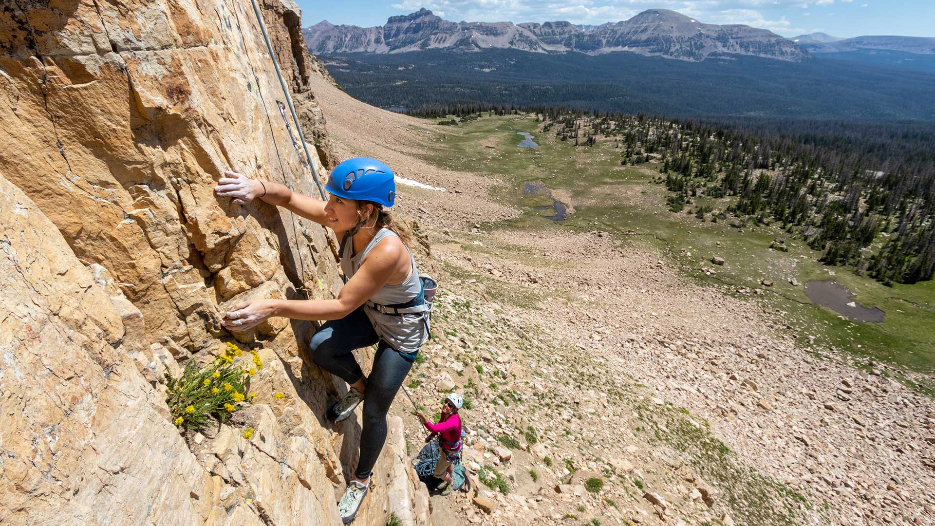 Person climbing a rocky mountain with scenic landscape in the background