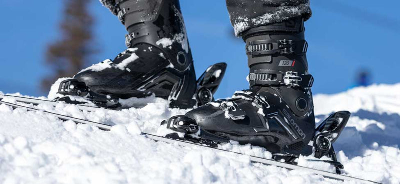 Close-up of ski boots attached to skis with snow and blue sky in the background