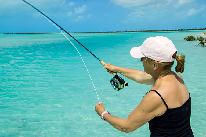 Woman fishing in clear blue water with a white cap and black tank top.